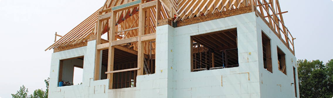 A house under construction with a second-story wooden frame over a first-floor structure insulated with foam boards.