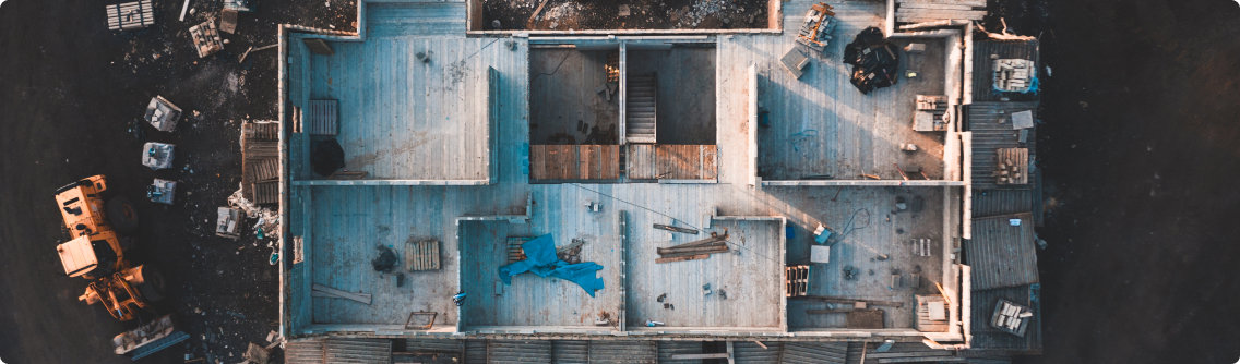 An aerial shot of an old industrial rooftop scattered with debris, machinery, and signs of wear, captured during the low light of dawn or dusk, highlighting the abandonment of the area.